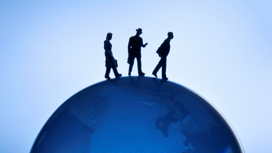 Figurines walking atop blue globe on blue background.