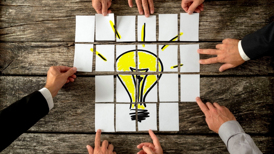 44155179 - high angle view of businessmen hands touching white papers arranged on a rustic wooden table forming a yellow light bulb. conceptual for bright business ideas and innovations.