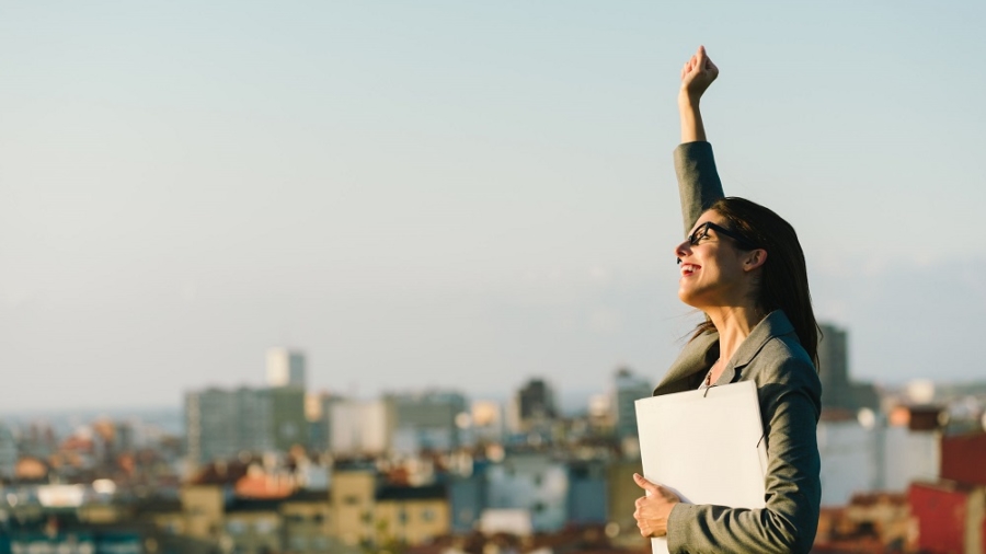 35777792 - successful young businesswoman raising arm celebrating business  or job achievement towards city background. professional happy woman walking outside.