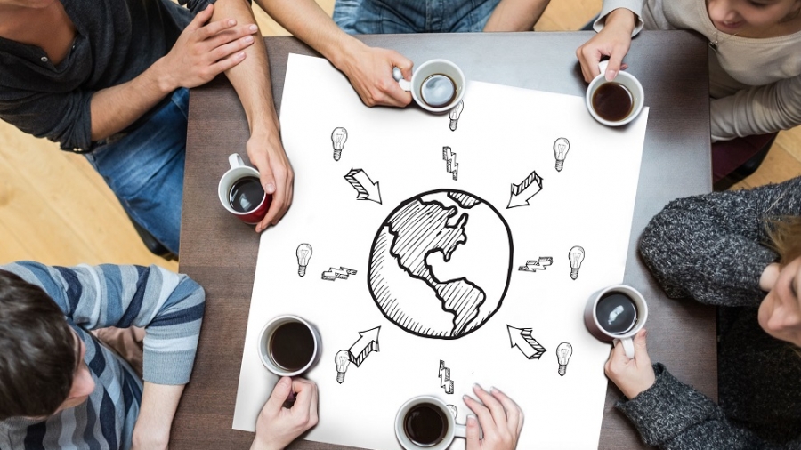 People sitting around table drinking coffee with page showing earth doodle with arrows